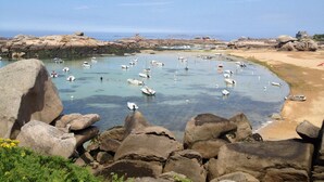 Escena costera con aguas cristalinas, embarcaciones y grandes rocas.