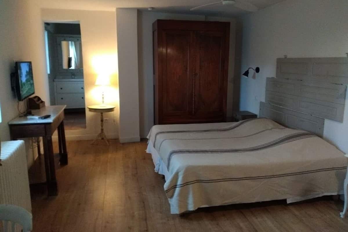 Un dormitorio con un armario de madera, una cama con cubrecama a rayas, una mesita de noche, una lámpara y un televisor sobre un mueble.