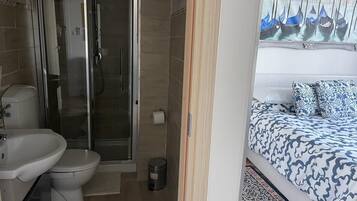 A bathroom with a shower, toilet, sink, and a trash bin.