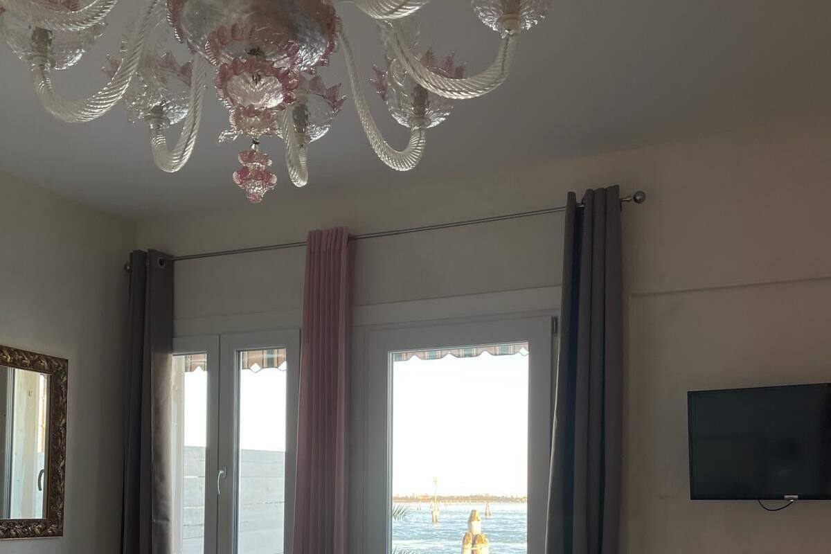 A hotel room with a bed, a dining table, chairs, a television, a small refrigerator, and a view of the sea through the window.