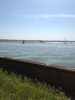 A river with a concrete barrier in the foreground and a distant shoreline with sparse vegetation. - Casa Sulla Laguna (Venice)