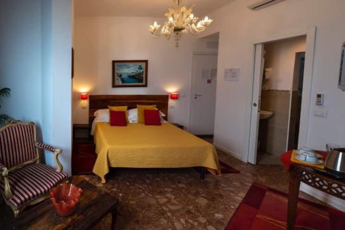 A bedroom with a bed, a chandelier, a painting, and a bathroom door.
