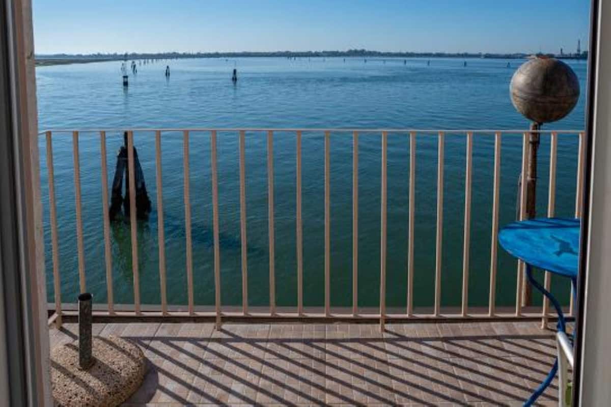 A balcony with a view of a calm body of water, a railing, and a small round table.