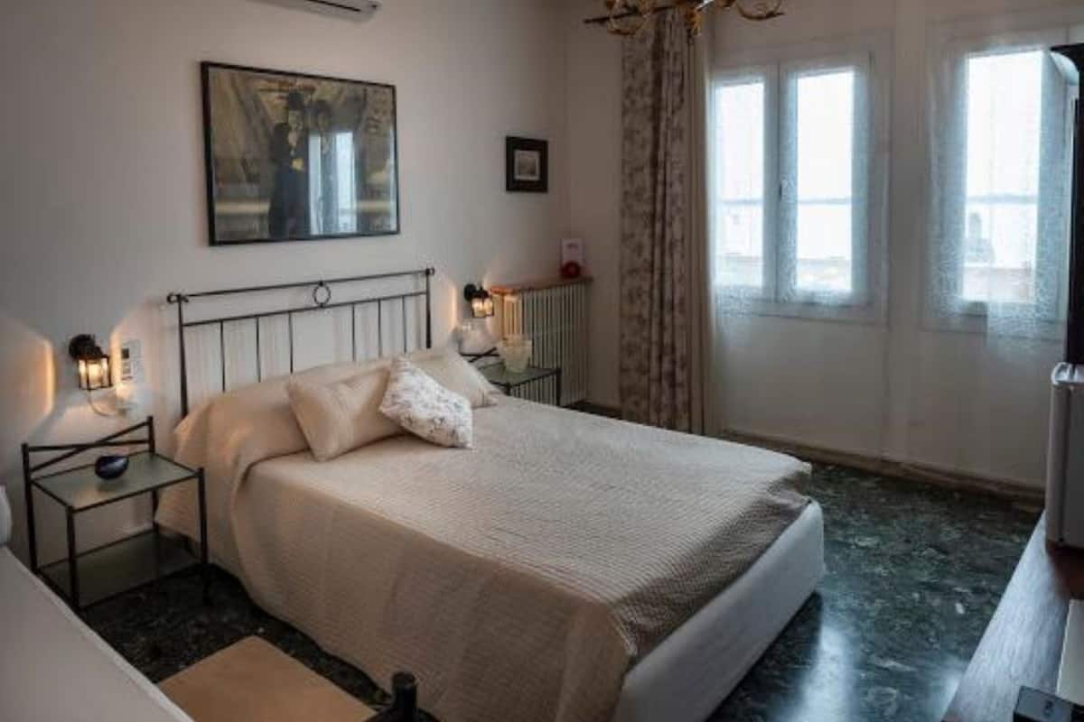 A bedroom with a bed, bedside tables, a lamp, a painting on the wall, and a window with curtains.