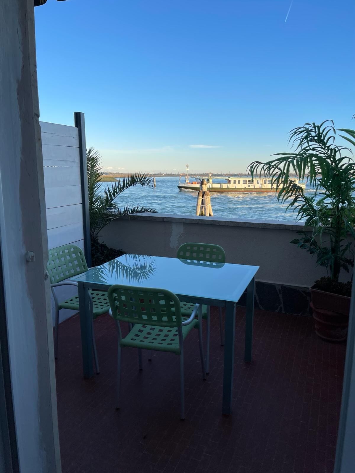 Un balcón con mesa y sillas, con vista a una masa de agua con barcos y una costa distante.