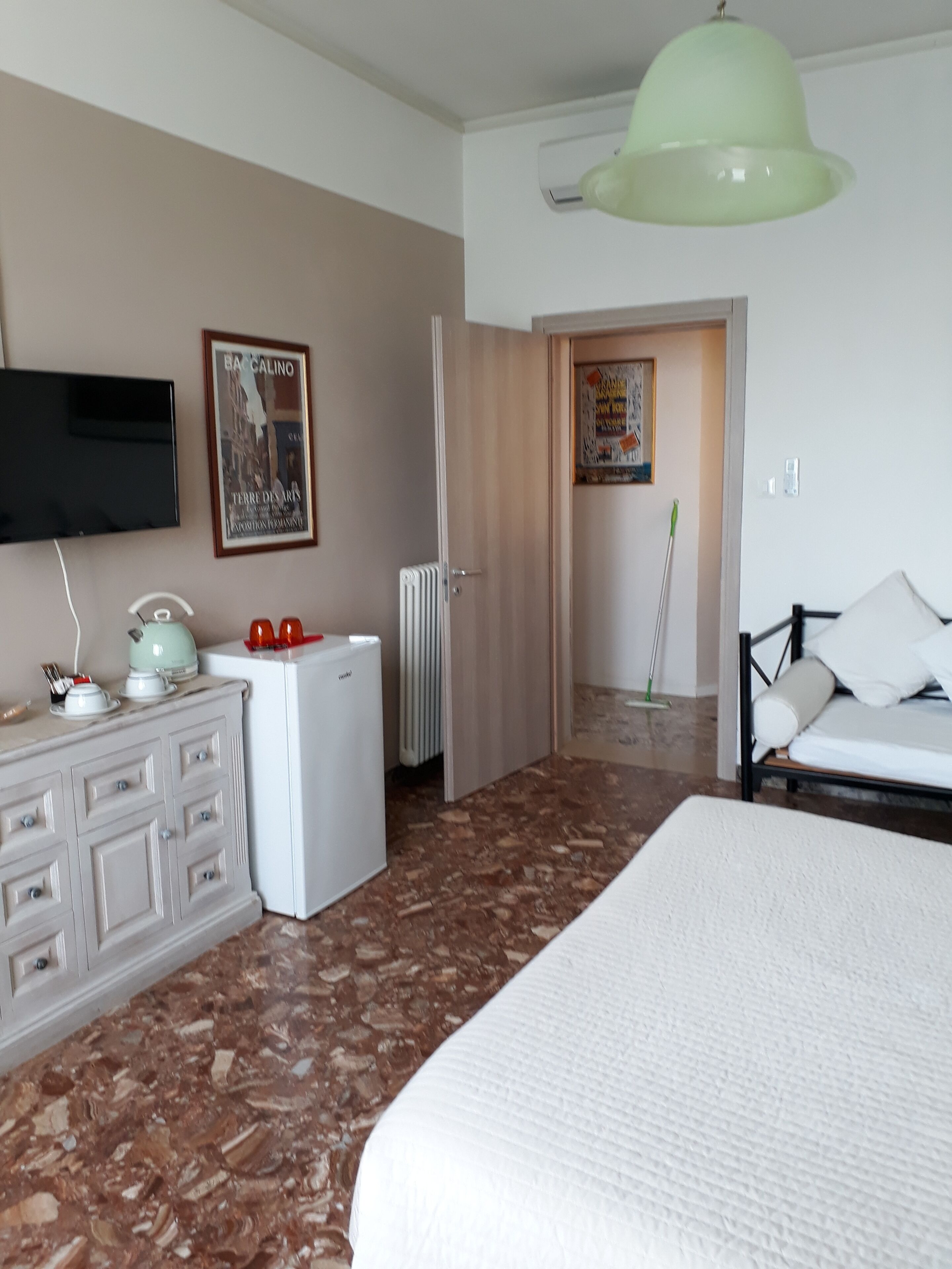 Ein Hotelzimmer mit Bett, Kommode, Heizkörper, Fernseher und einer grünen Deckenleuchte.