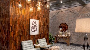 Un espace de détente moderne avec des murs lambrissés en bois, deux fauteuils gris rembourrés, une table ronde en bois agrémentée d’objets décoratifs et un lampadaire.