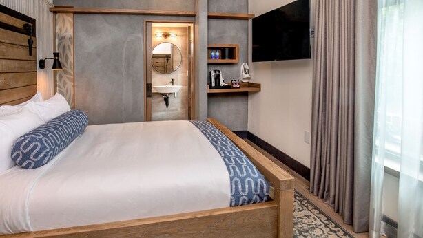 A hotel room with a wooden bed, a built-in sink, a television, and a bathroom mirror. - Hotel 1868 (Cambridge)