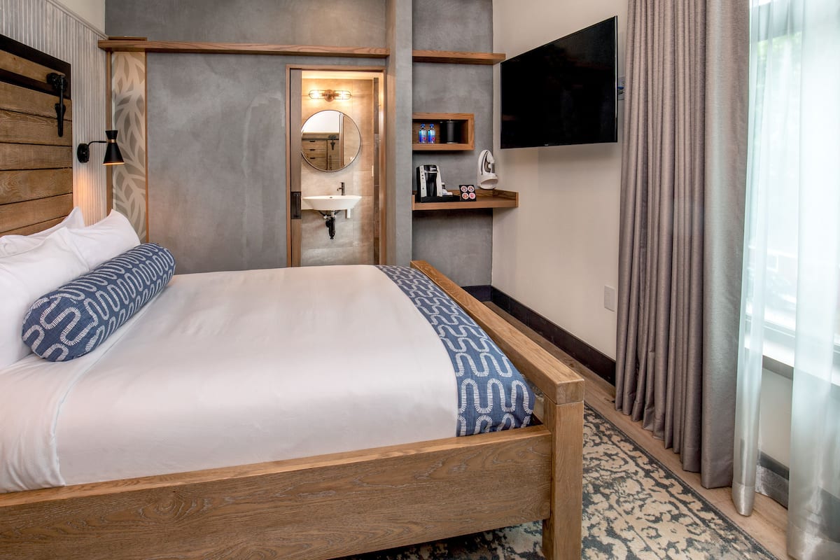 A hotel room with a wooden bed, a built-in sink, a television, and a bathroom mirror.