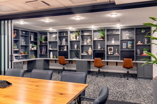 A conference room with a wooden table, grey chairs, and shelves with decorative items.