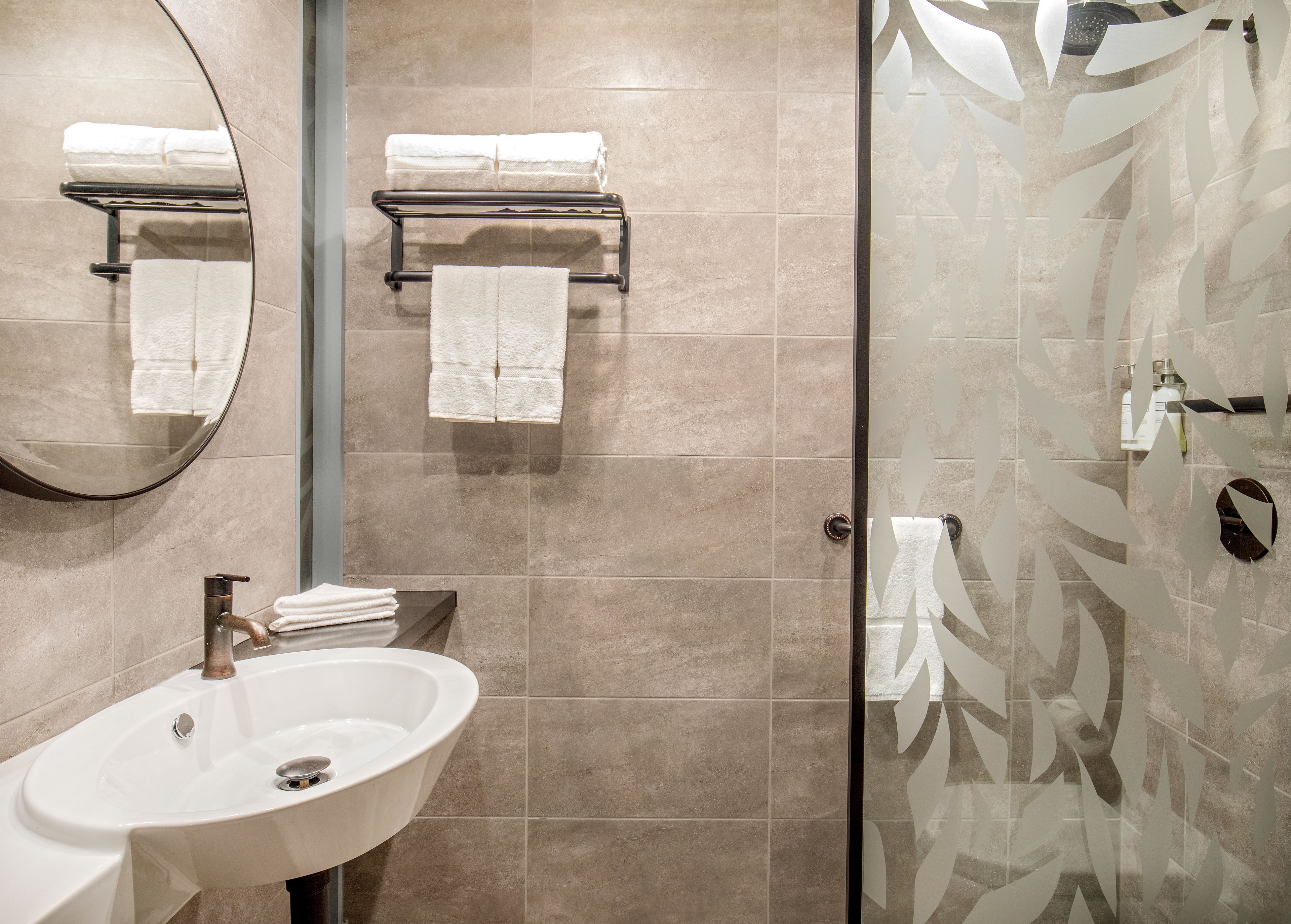 Un bany modern amb un lavabo, un mirall, una barra de tovalloles i una porta de dutxa de vidre.