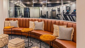 Une salle de sport moderne avec un banc en cuir marron aux lignes courbes, de petites tables rondes et des poufs en fibres tressées.