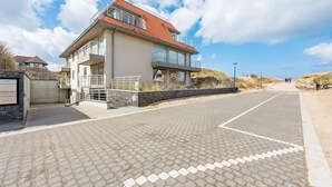 A modern building with a red roof, a balcony, and a paved walkway leading to it. - Zeegerucht Duplex (Koksijde)