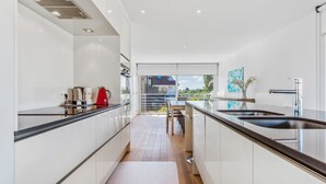 A modern kitchen with white cabinets, a wooden floor, a red kettle, and a view of the outdoors. - Zeegerucht Duplex (Koksijde)
