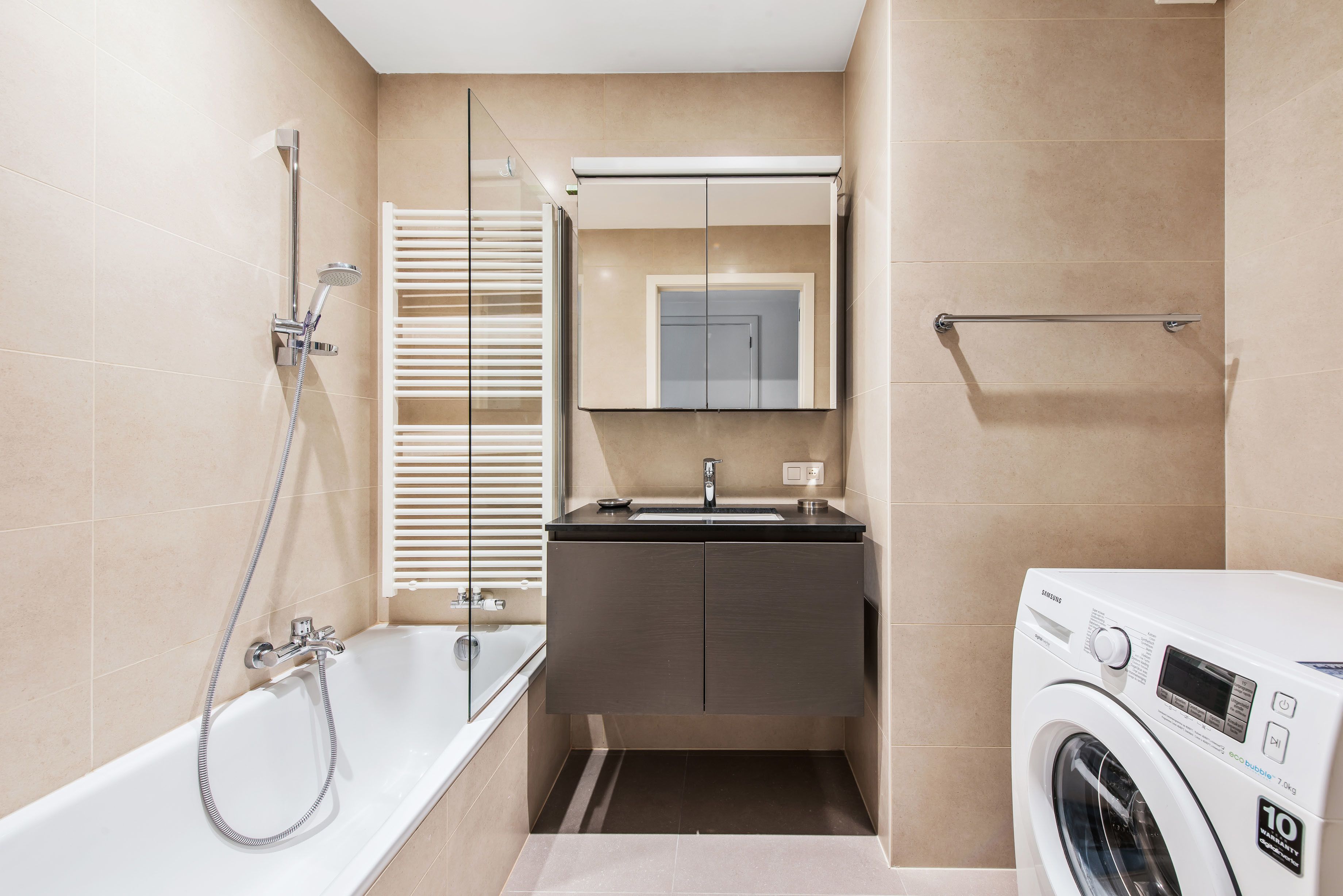 Un baño moderno con bañera, lavamanos integrado, espejo y lavadora.