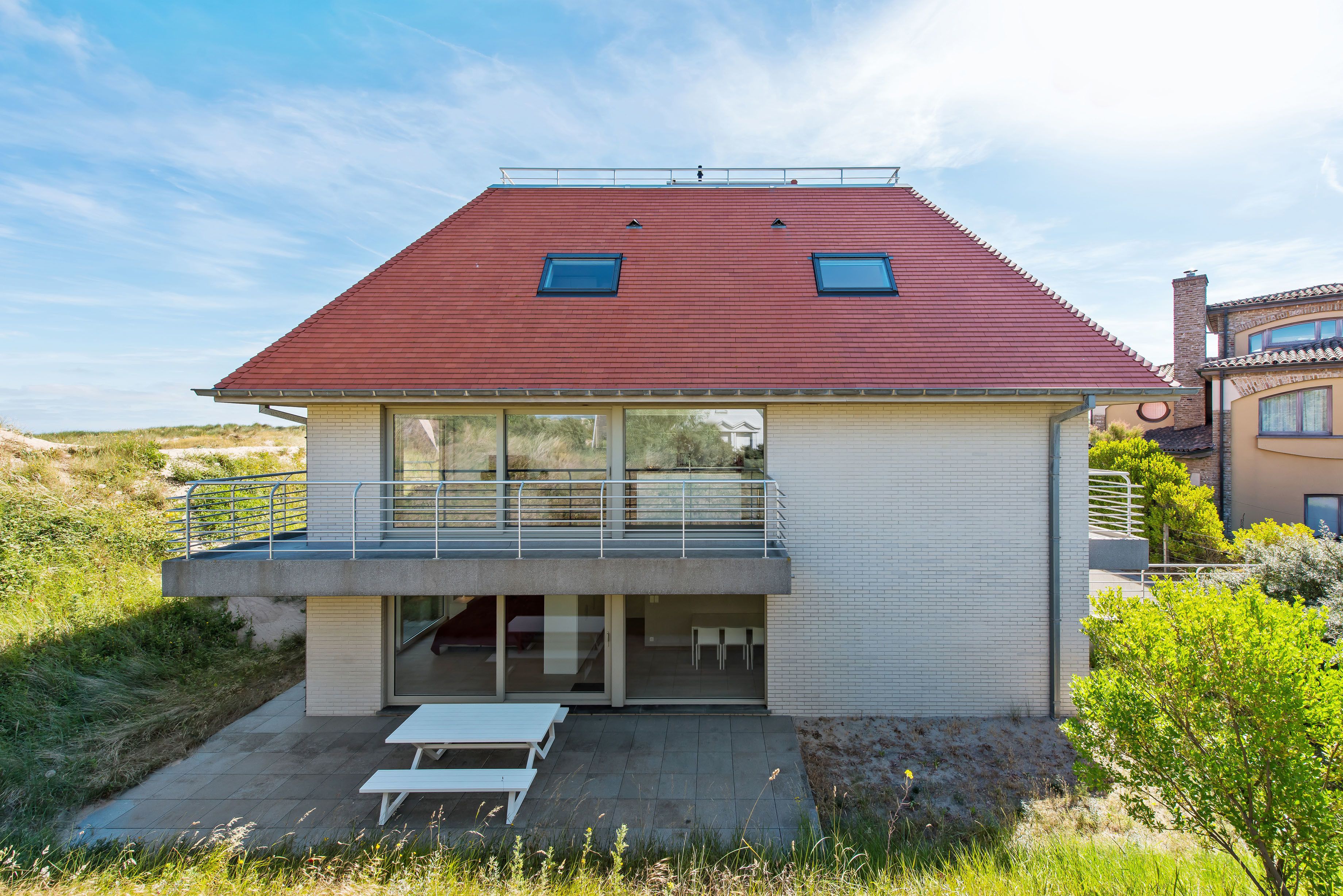 A modern house with a red roof, a balcony, and a patio area.