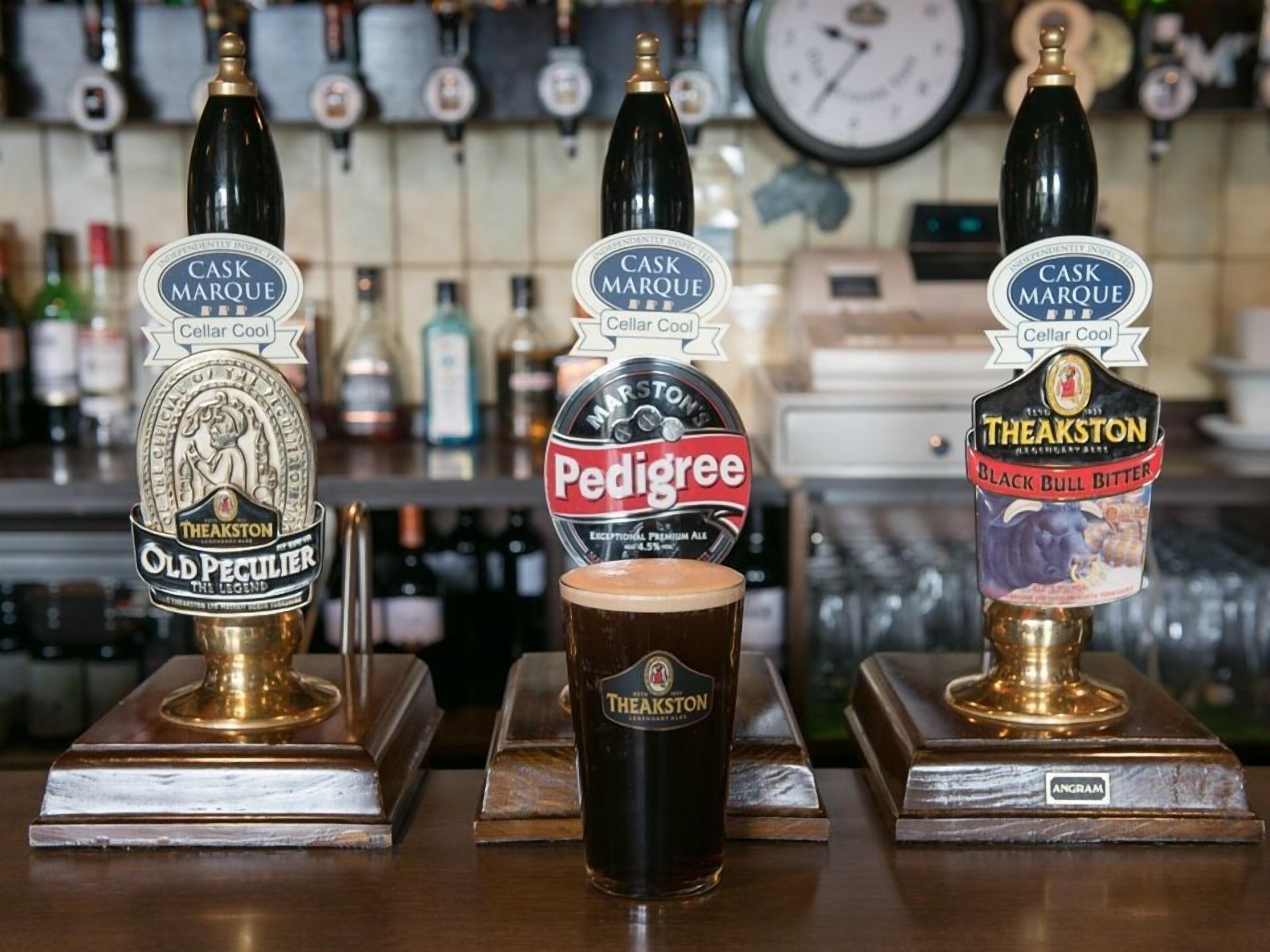 A bar with three taps labeled 'Cask Marque', 'Pedigree', and 'Theakston'. A glass of beer is in front of the 'Pedigree' tap.