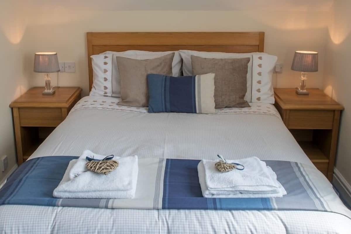 Un letto rifatto con cura, con una coperta a righe, due cuscini e due asciugamani piegati ai piedi. Due comodini con lampade sono posti su entrambi i lati del letto.