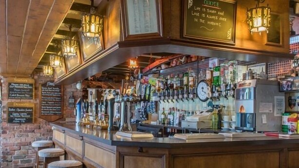 Uma área de bar com balcão de madeira, várias torneiras e banquetas.