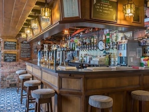 A bar area with a wooden counter, multiple taps, and stools.