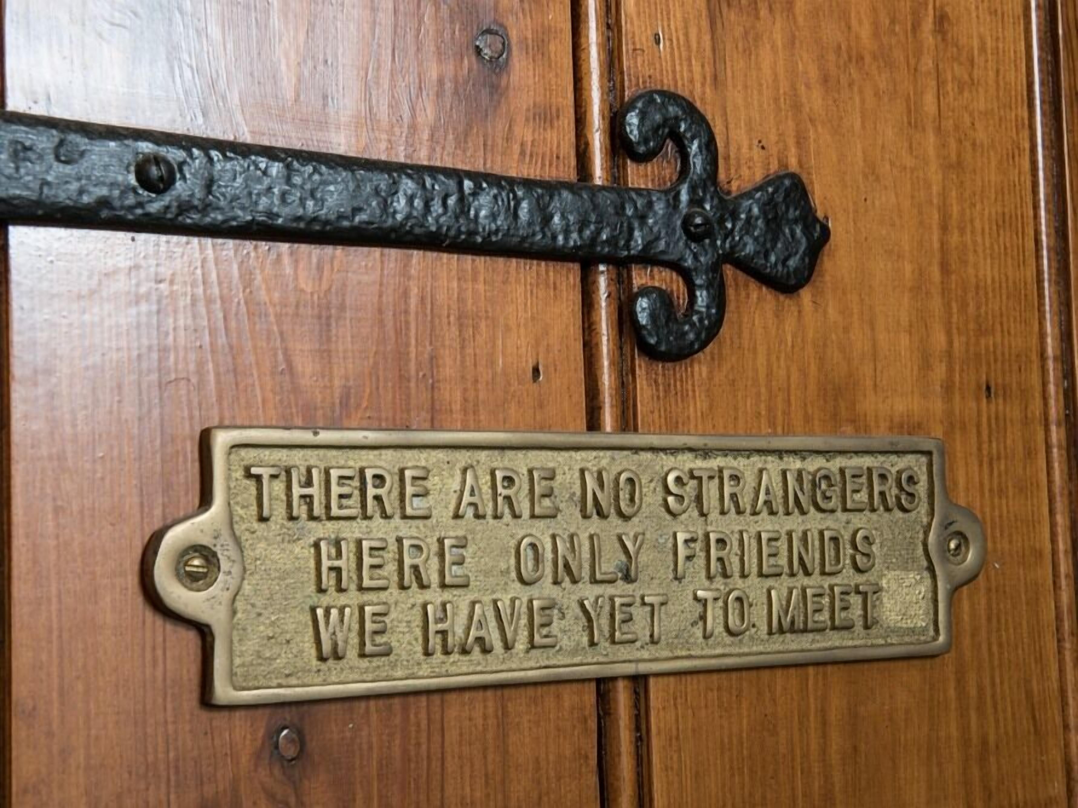 Una puerta de madera con una placa de metal que dice "AQUÍ NO HAY EXTRAÑOS, SÓLO AMIGOS QUE AÚN NO CONOCEMOS."