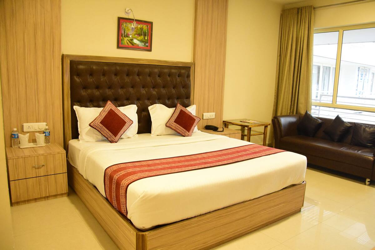 A hotel room with a large bed, a leather sofa, a small table, and a window with curtains.