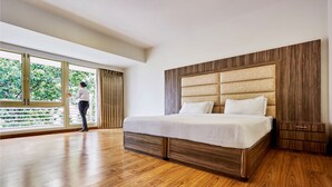 Quarto espaçoso com uma cama grande, piso de madeira e vista para o verde através de uma janela ampla.