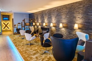 Un interior moderno con pared de piedra, varias sillas y una recepción con una gran 'X' iluminada.