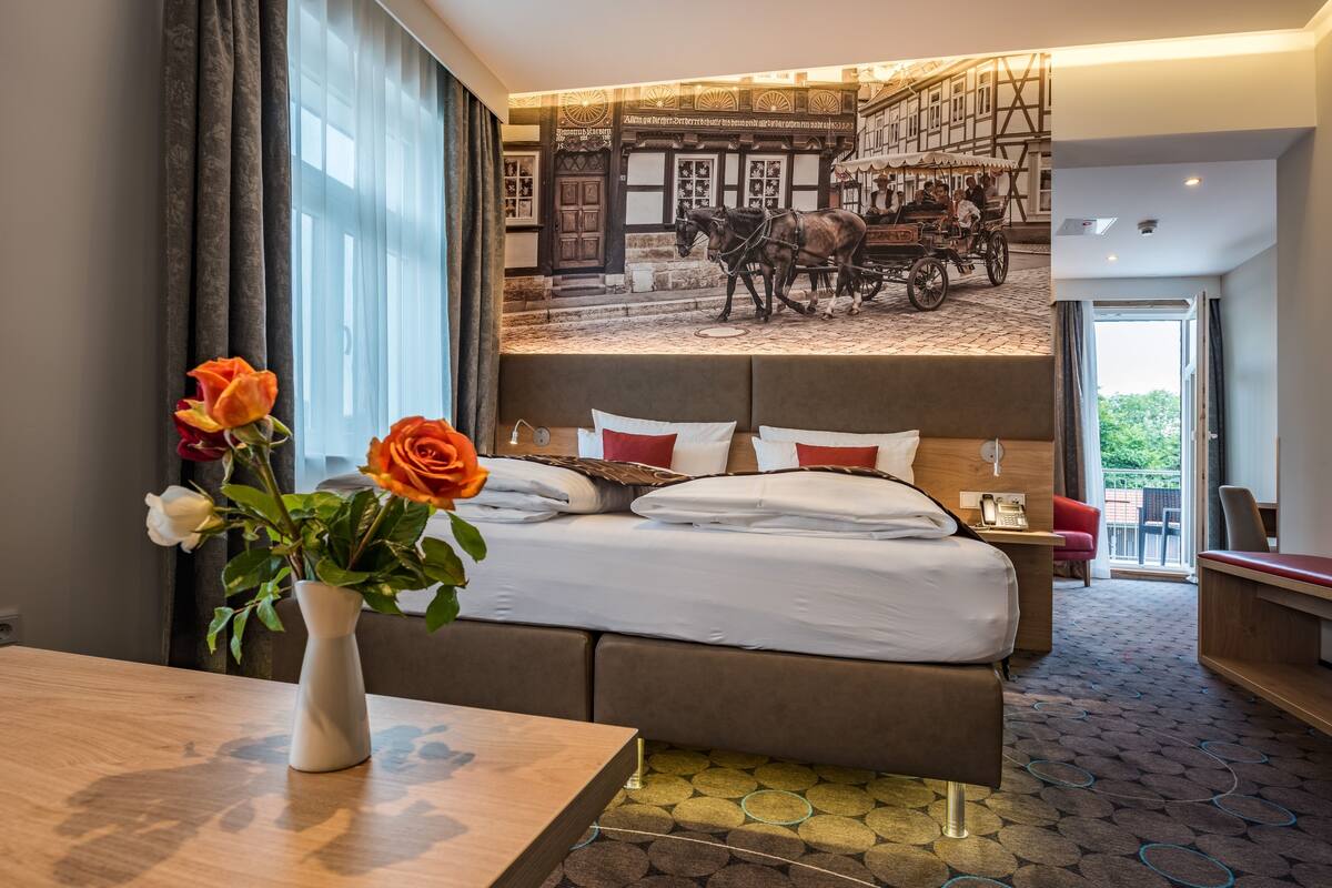 Ein Hotelzimmer mit einem großen Bett, einem Blumenstrauß und einem Wandgemälde einer Kutsche.