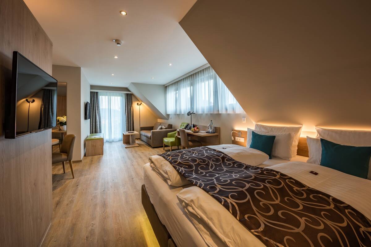 Ein modernes Hotelzimmer mit einem großen Bett, einem Schreibtisch, einem Sessel und einem Fernseher.