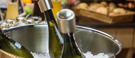 Un recipiente metálico con botellas de vino y hielo, rodeado de diversos alimentos y aderezos.