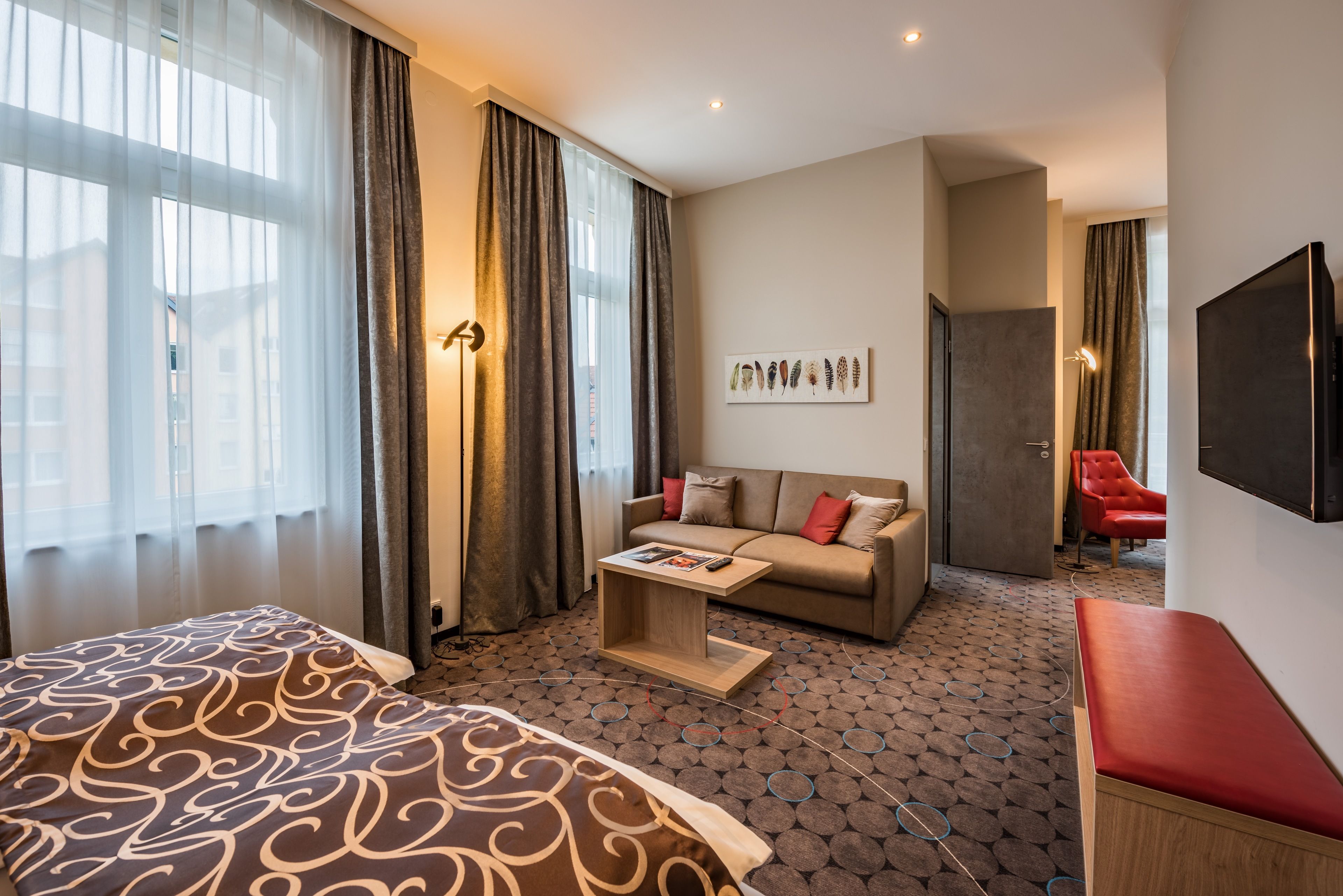 A hotel room with a bed, a sofa, a small table, and a TV.
