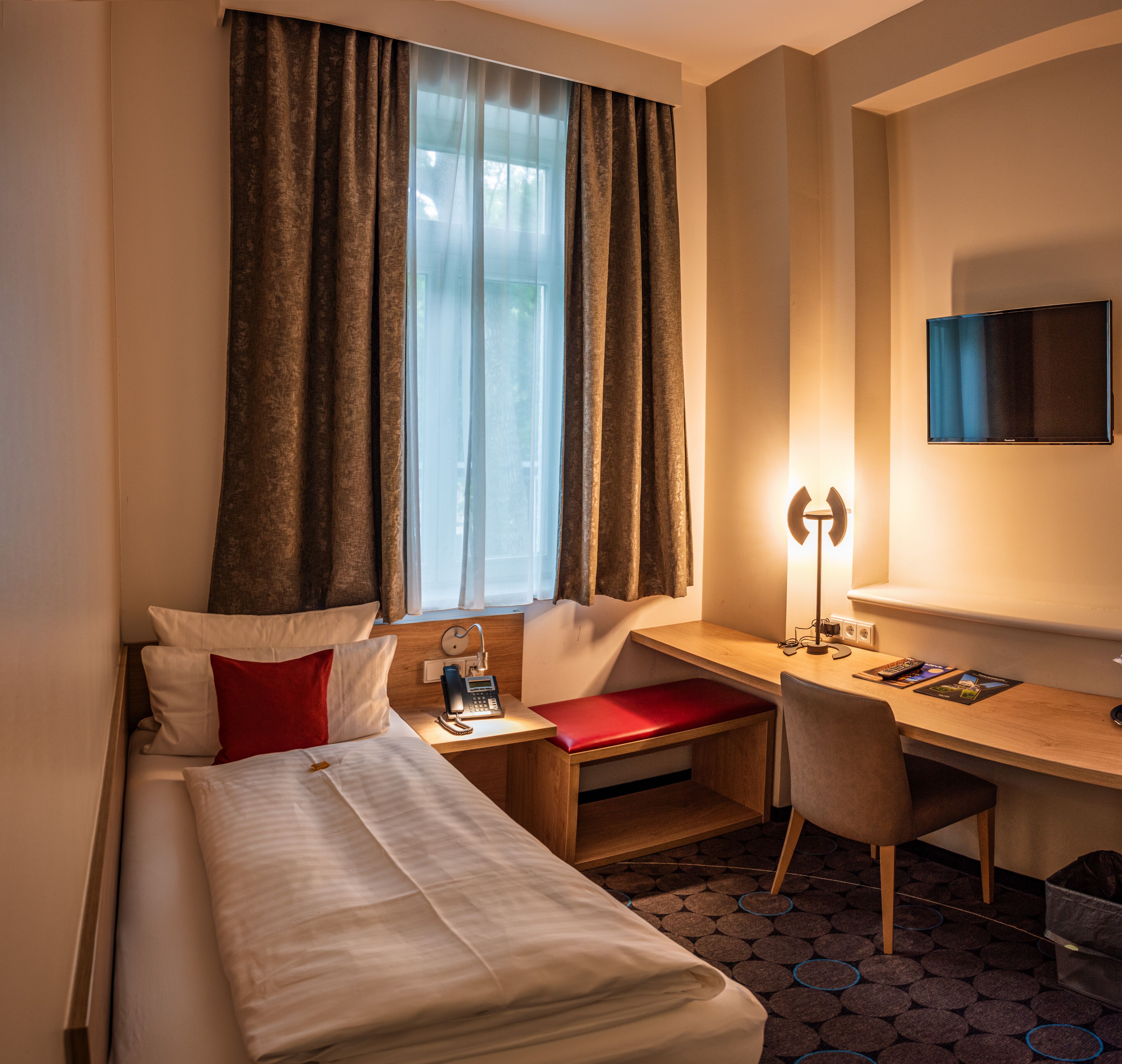 Ein Hotelzimmer mit Bett, Schreibtisch, Stuhl, Telefon und Fernseher.
