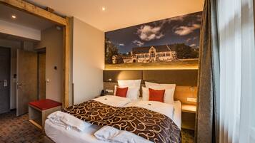Una habitación de hotel con una cama grande, un banco rojo, una mesita de noche y un televisor montado en la pared.