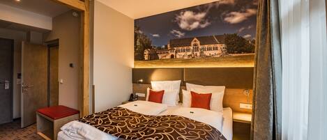 A hotel room with a large bed, a red bench, a nightstand, and a wall-mounted TV.