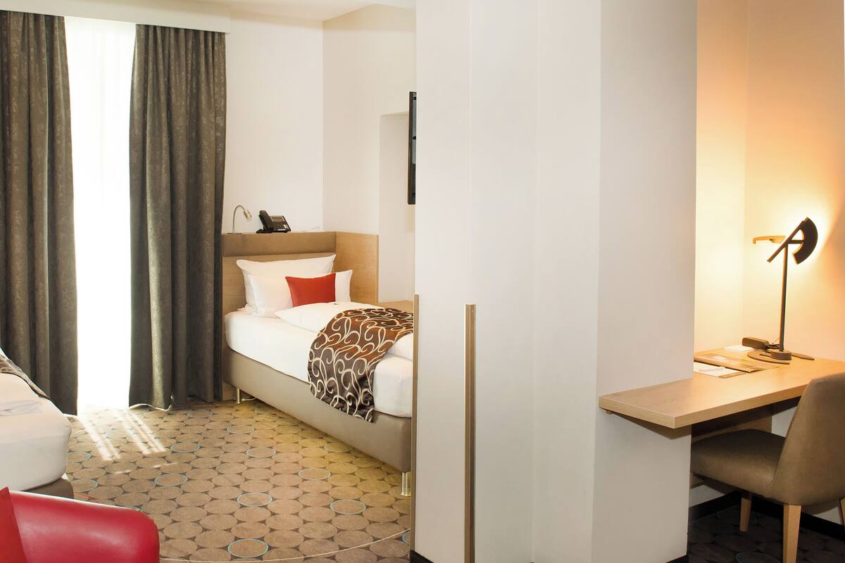 Ein Hotelzimmer mit zwei Betten, einem Schreibtisch, einem Stuhl, einer Lampe und einem Telefon.