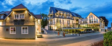 Ein mehrstöckiges Hotel im traditionellen europäischen Stil mit einem markanten Eingangsbereich, überdachter Parkgarage und einer gut beleuchteten Fassade.