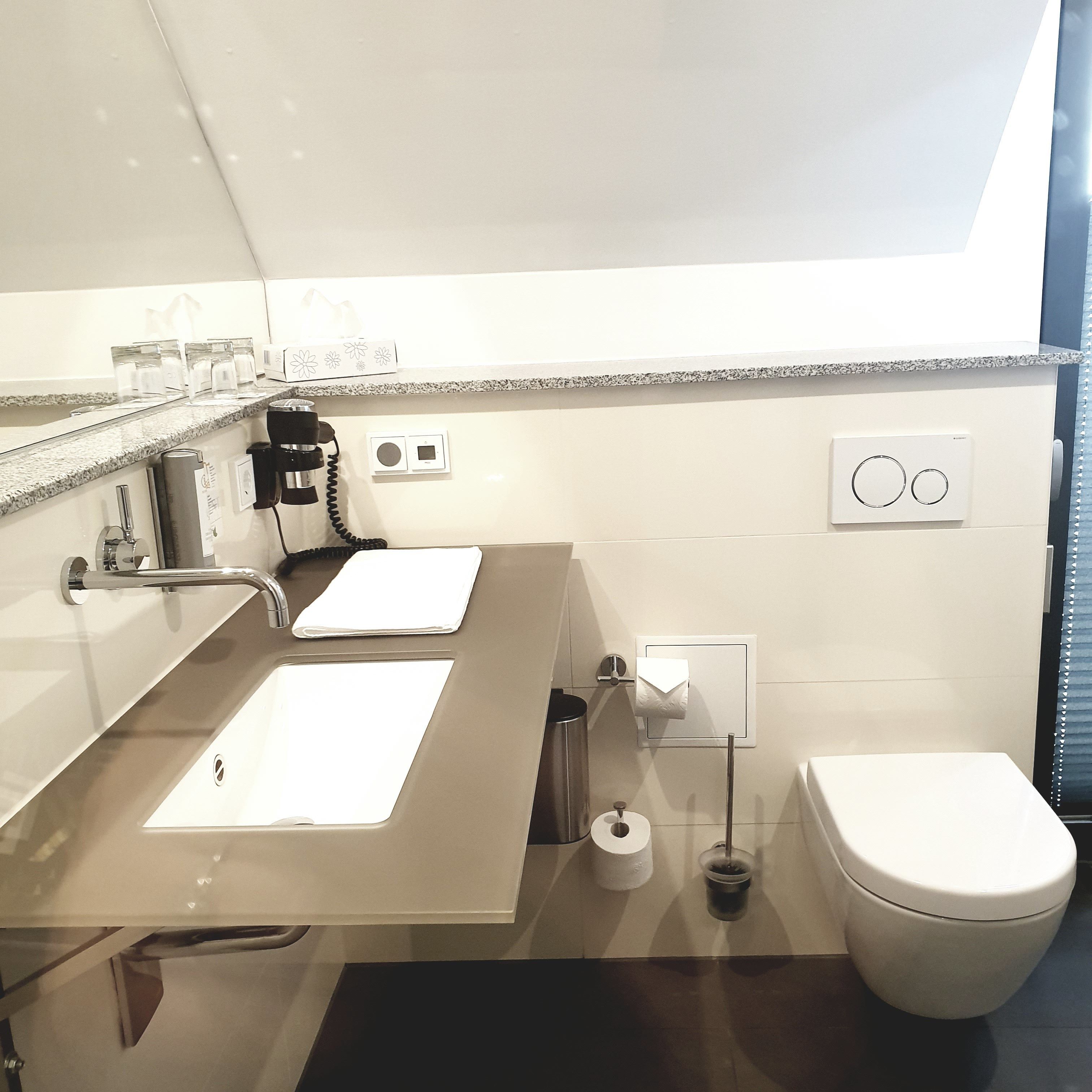 Un baño moderno con un espejo grande, dos lavamanos, un inodoro y un cesto de basura.