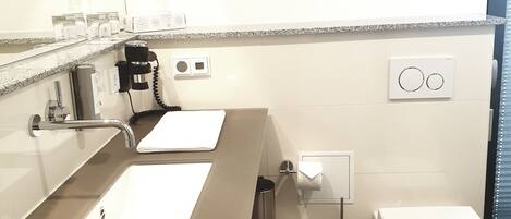 Un baño moderno con un espejo grande, dos lavamanos, un inodoro y un cesto de basura.