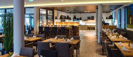A modern restaurant with wooden tables and chairs, a bar area, and large windows.