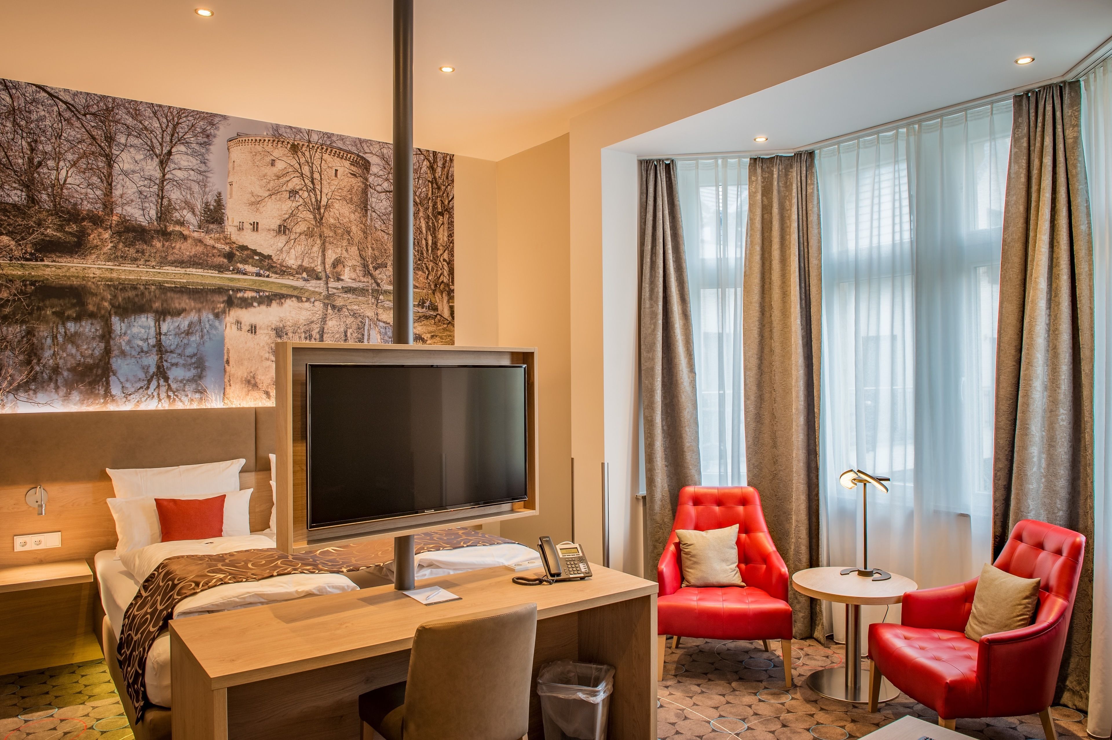Een hotelkamer met een bed, bureau, televisie en twee rode stoelen.
