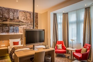 Une chambre d’hôtel avec un lit, un bureau, une télévision et deux chaises rouges.