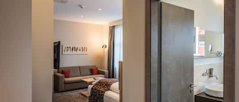 Une chambre d’hôtel moderne, équipée d’un lit, d’un canapé, d’une petite table et d’une salle de bain avec un lavabo et un miroir.