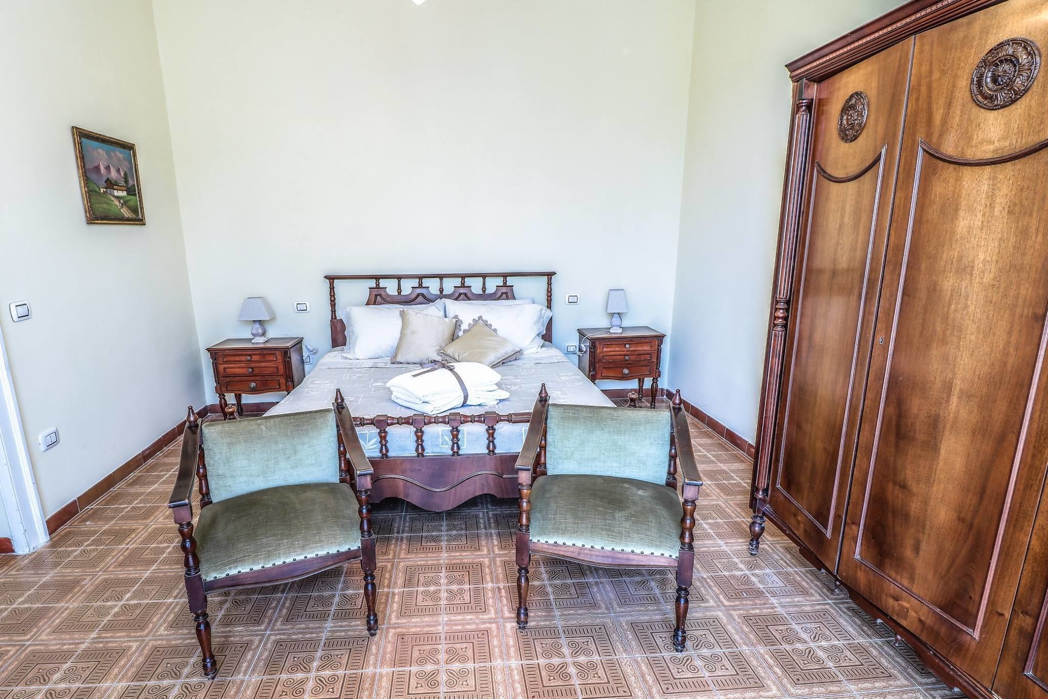 A bedroom with a large bed, two nightstands, a wooden wardrobe, and a dining table with chairs.
