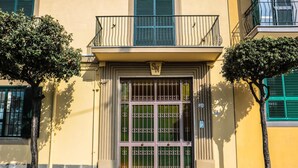 A building with a yellow facade, a large metal gate with a sign above it, and a balcony with green shutters. - Scognamiglio Suites (Ercolano)