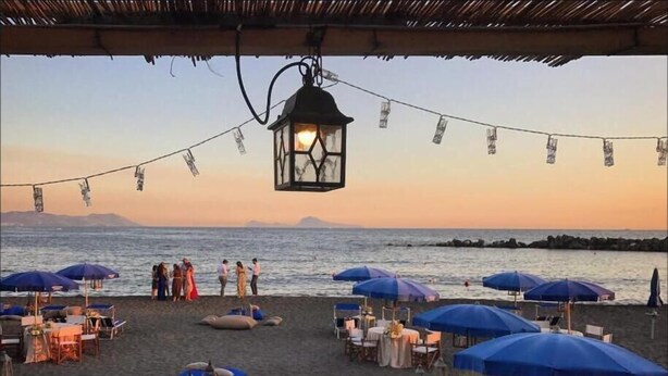 A beachside restaurant with tables and umbrellas, overlooking the sea. - Scognamiglio Suites (Ercolano)