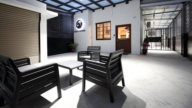 L’intérieur d’une auberge de jeunesse moderne, avec un plafond haut, un espace salon central et une porte d’entrée bien visible.