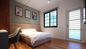Une chambre à coucher avec un lit, une chaise, une fenêtre et des œuvres d’art accrochées au mur.