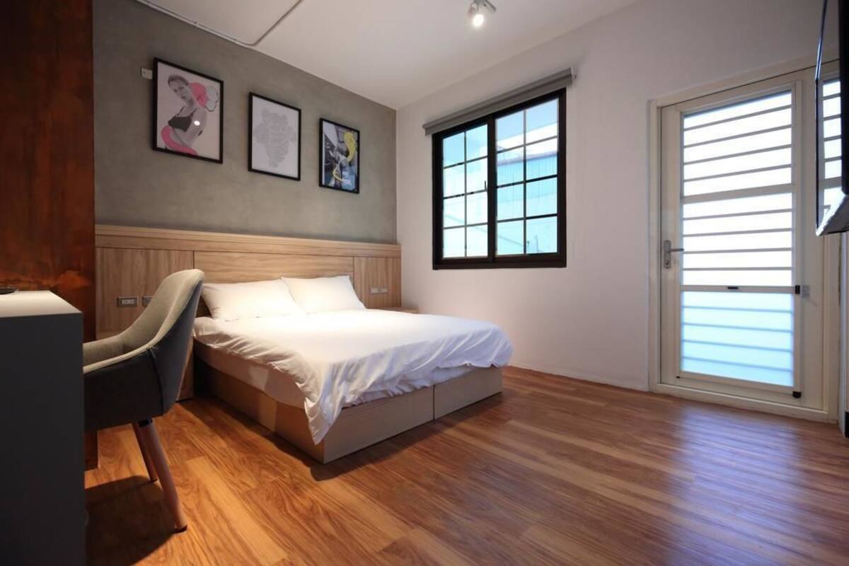 A bedroom with a bed, a chair, a window, and artwork on the wall.