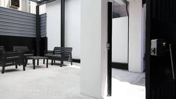 A modern interior with a seating area featuring black chairs and a table, a white wall, and a metal-framed window.